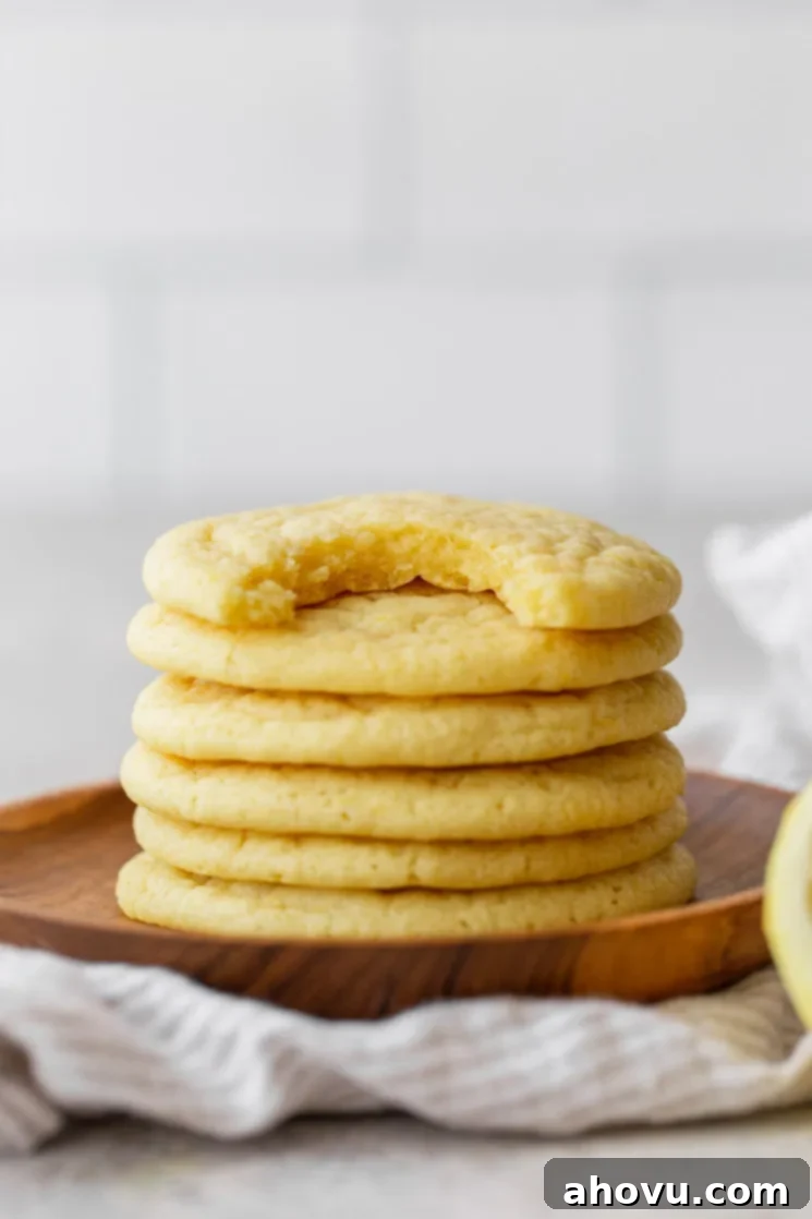 A delectable stack of soft lemon cookies arranged on a wooden plate, with the top cookie featuring a tempting bite taken out, revealing its fluffy interior.