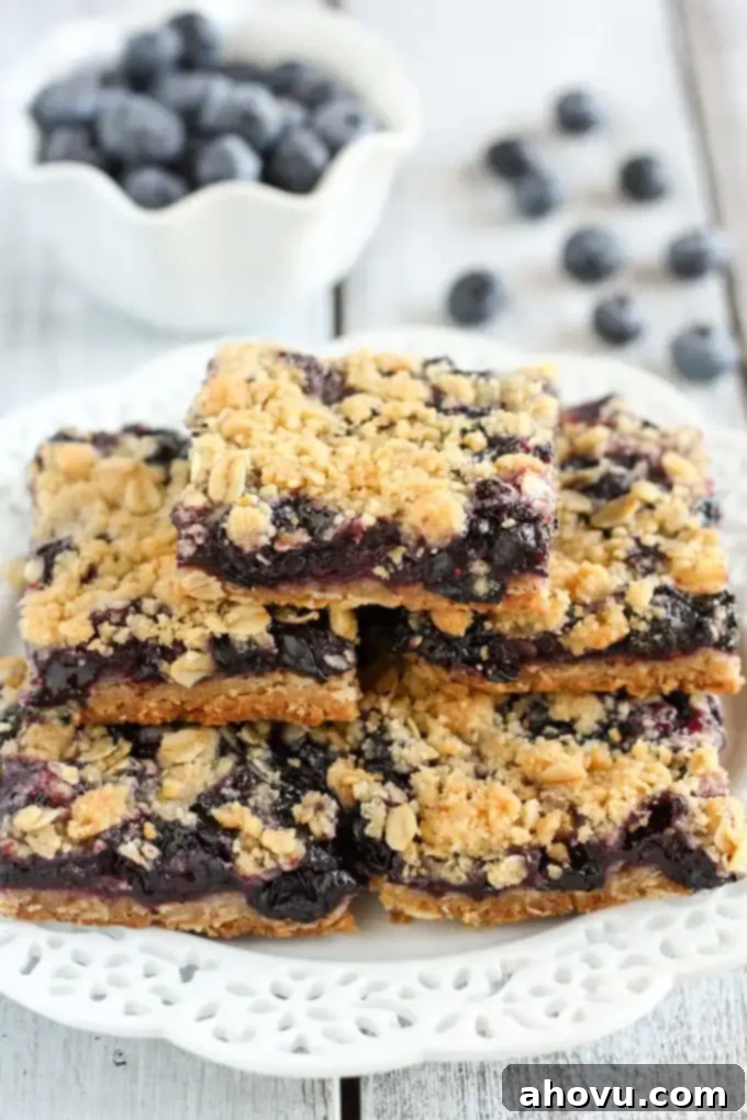 A stack of blueberry crumble bars on a white plate with a dish of fresh blueberries in the background. 