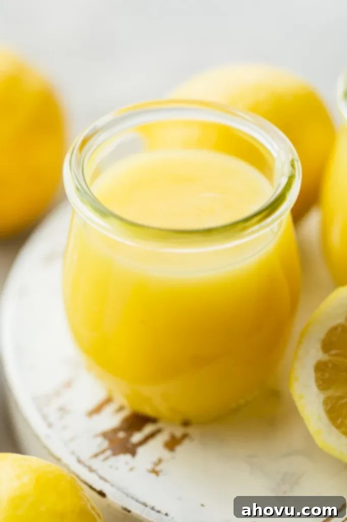 A small glass jar filled with microwave lemon curd sitting on top of a worn white wood surface.