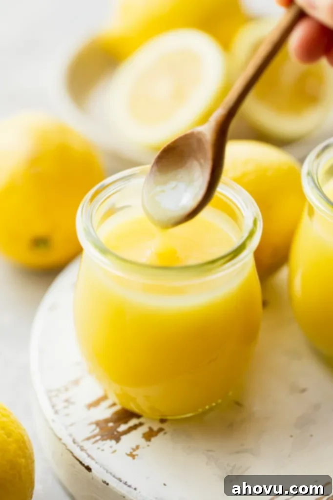 A wooden spoon scooping lemon curd out of a small glass jar.