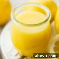 A small glass jar filled with lemon curd on top of a worn white wood surface.