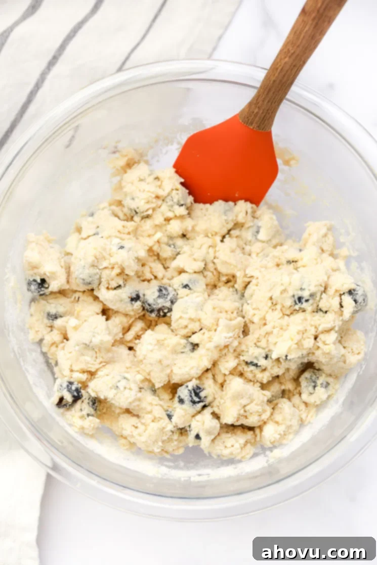 A large glass bowl filled with the dough for lemon blueberry scones and a rubber spatula on the side.