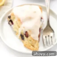A closeup shot of a lemon blueberry scone on a white plate with a fork on the side.
