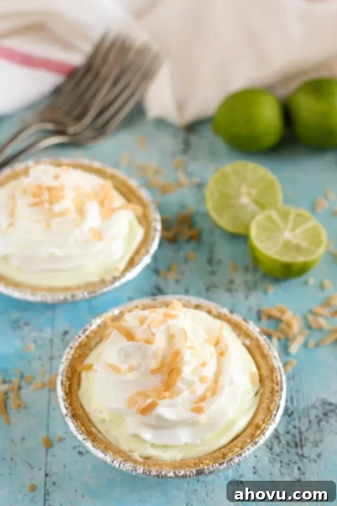 Multiple Mini Key Lime Greek Yogurt Cheesecake Pies on a tray, garnished with whipped cream and toasted coconut