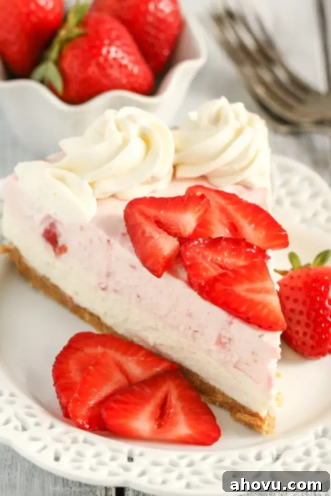 A slice of no bake strawberry cheesecake on a white dessert plate with berry slices. A dish of berries and a fork rest in the background. 