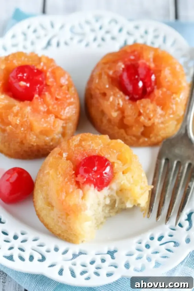 Caramelized Pineapple Mini Cakes 4 Three perfectly formed individual pineapple upside down cakes on a white plate with a fork. One mini cake shows a small bite taken, revealing the tender cake texture.