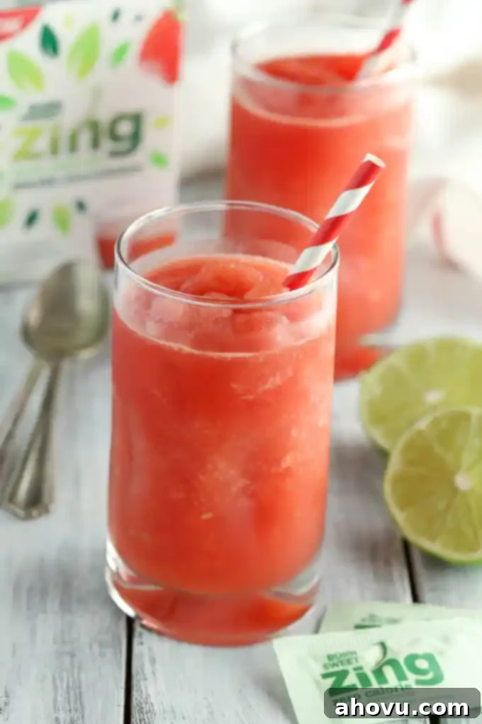 Watermelon Zest Cooler 2 A vibrant pink watermelon lime slushie in a clear glass, garnished with a fresh lime slice, against a soft-focus background.