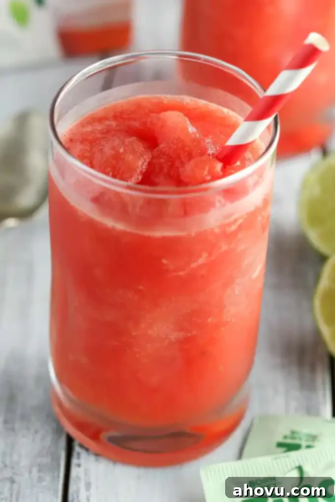 Watermelon Zest Cooler 5 A close-up of a refreshing watermelon lime slushie in a textured glass, adorned with a vibrant green lime slice and showing the frosty, thick consistency.
