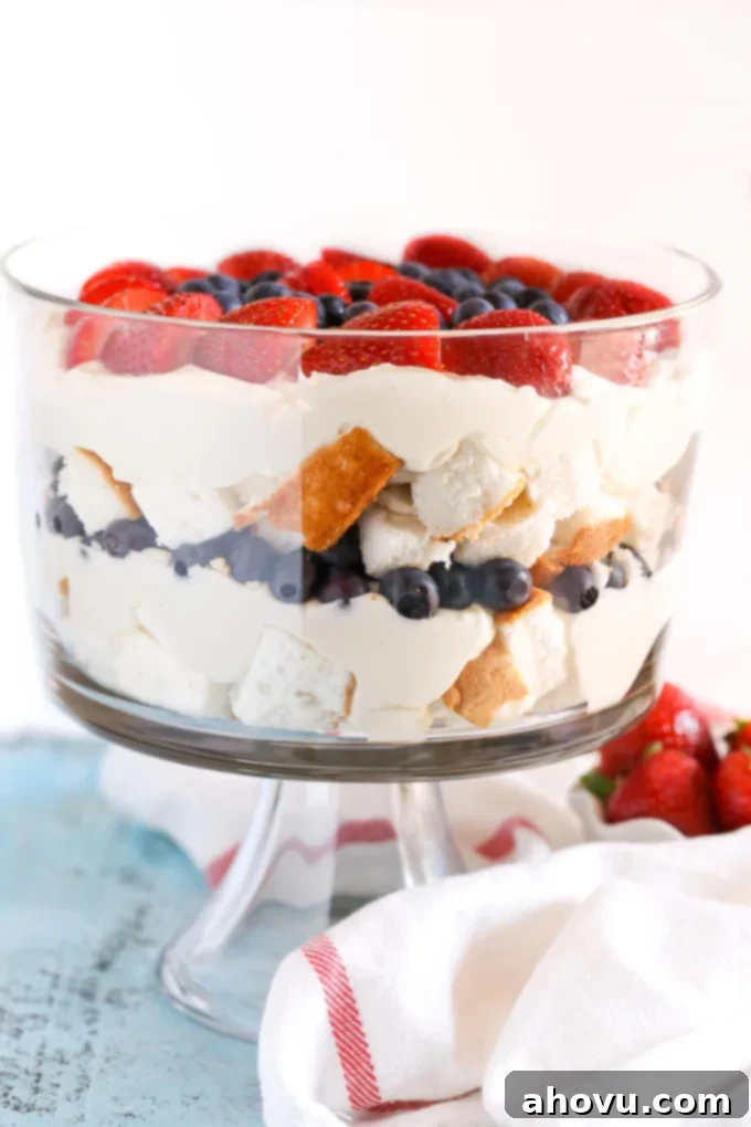 Side view of a large berry trifle in a glass trifle dish, showcasing distinct layers of cake, cream, and berries.