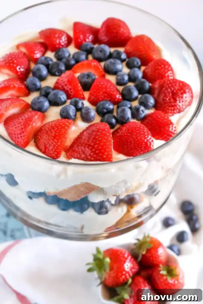 Top view of a berry trifle garnished with fresh strawberries and blueberries, with a small dish of strawberries in the foreground, highlighting the fresh fruit component.