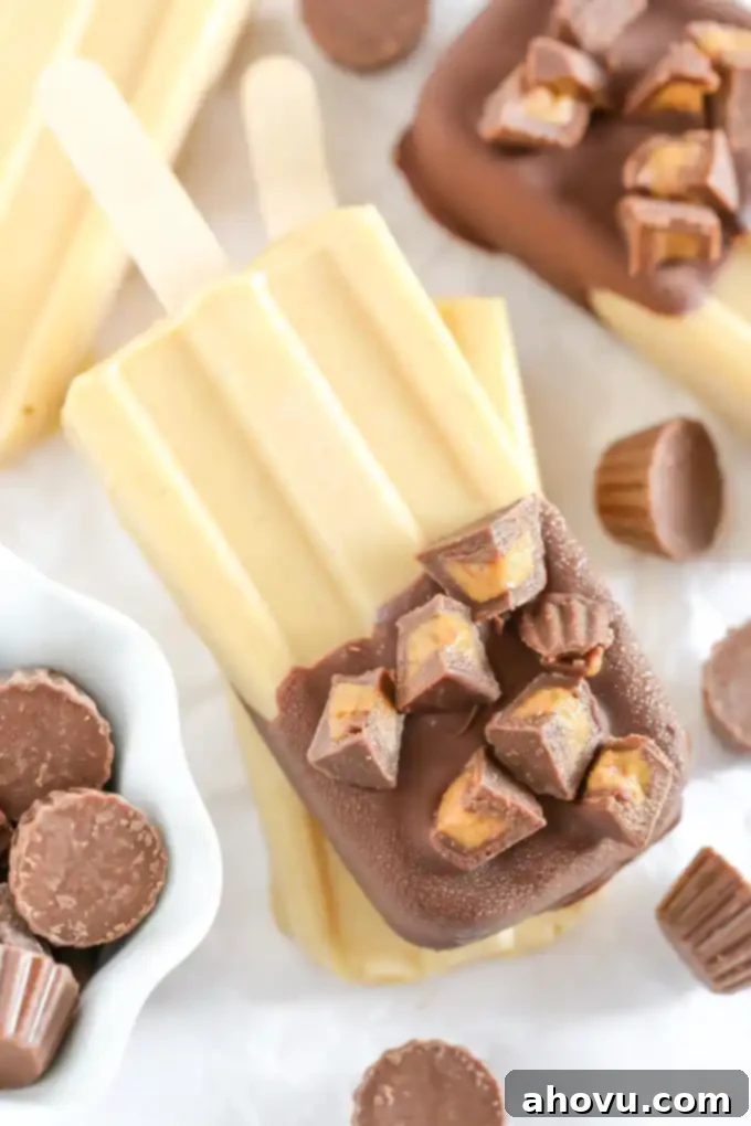 Creamy peanut butter popsicles generously coated with chocolate magic shell and adorned with mini peanut butter cups, presented as a delicious and easy summer treat