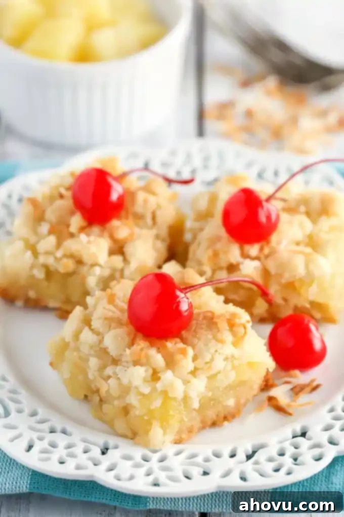 Three golden-brown coconut pineapple bars, beautifully garnished with bright red maraschino cherries, presented on an elegant white dessert plate. A small, inviting bowl of fresh pineapple chunks sits gently blurred in the background, hinting at the key ingredient.
