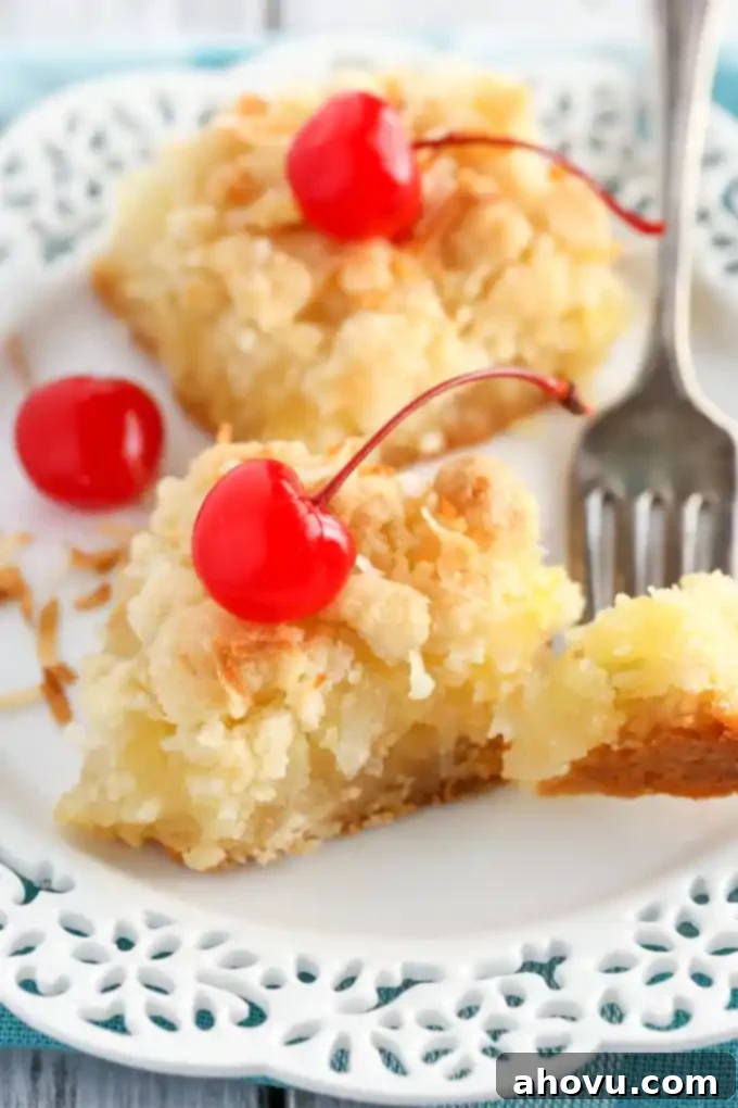 A close-up of two perfectly cut coconut pineapple bars, one of which has a piece gently lifted by a fork, revealing the luscious, golden pineapple coconut filling and the distinct layers of crumbly crust and topping. The bars are presented on a white dessert plate, highlighting their appetizing texture.