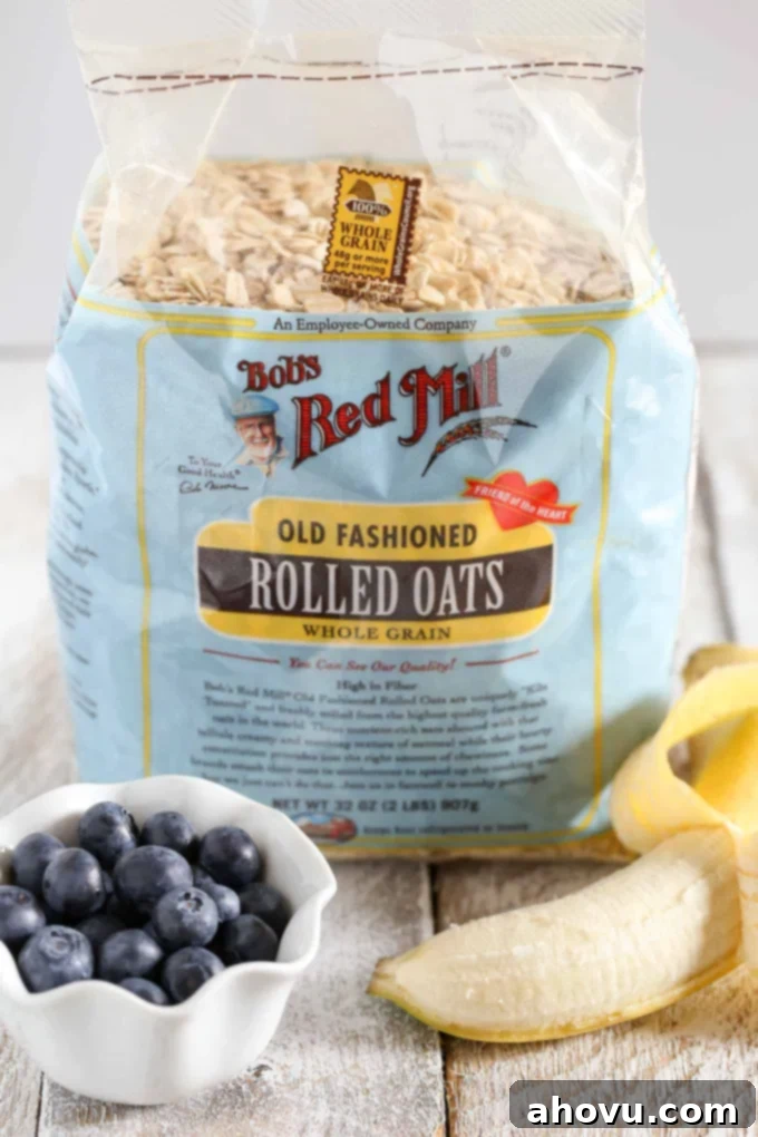 Essential ingredients for Blueberry Banana Baked Oatmeal: a small dish of fresh blueberries, a bag of old-fashioned rolled oats, and a partially peeled ripe banana on a clean white surface.