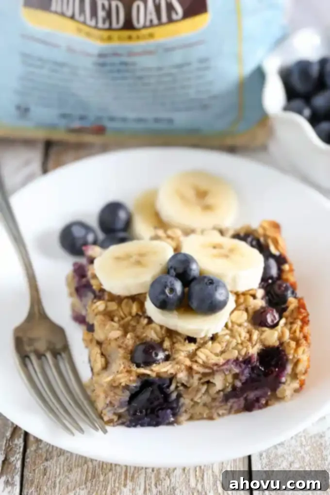 A perfectly sliced piece of banana blueberry baked oatmeal, elegantly garnished with fresh banana slices and whole blueberries, presented on a white plate with a fork.