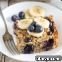 A top-down view of a serving of Blueberry Banana Baked Oatmeal, garnished with fresh blueberries and banana slices, on a light plate.
