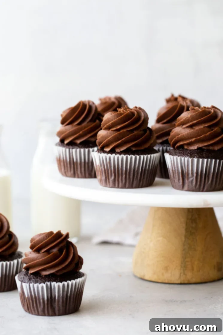 A marble cake stand holding chocolate cupcakes topped with chocolate frosting with jugs of milk in the background.