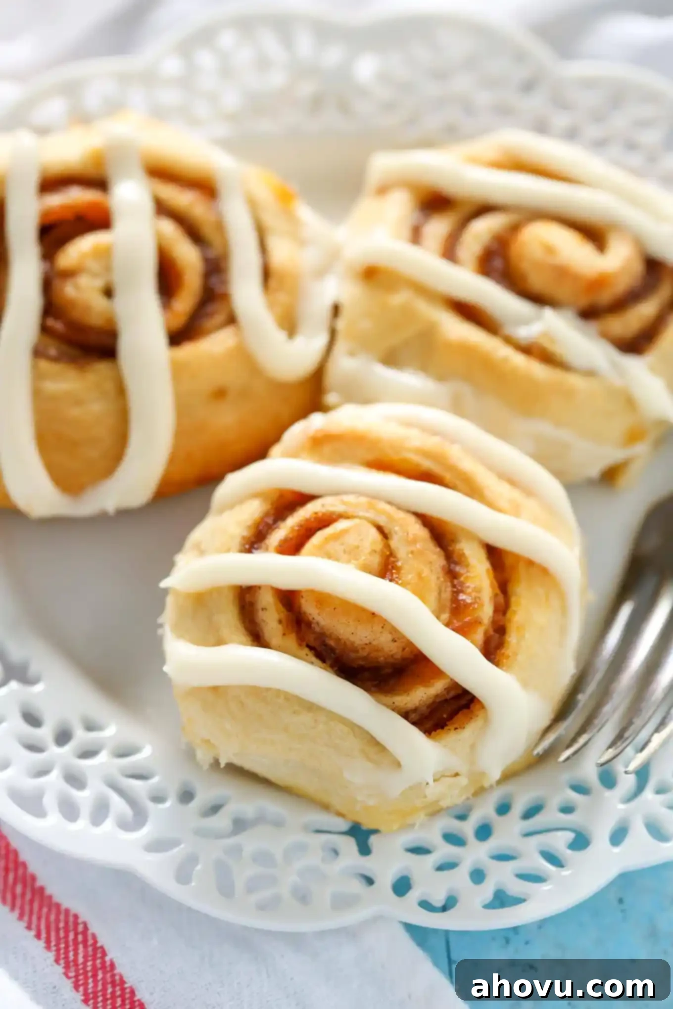 Three iced pumpkin cinnamon rolls on a white plate, showcasing their soft texture and creamy frosting.