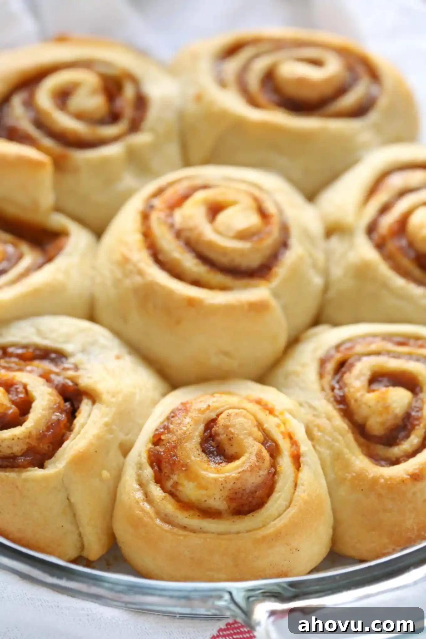 A pie plate of baked pumpkin spice cinnamon rolls waiting to be iced with cream cheese frosting.