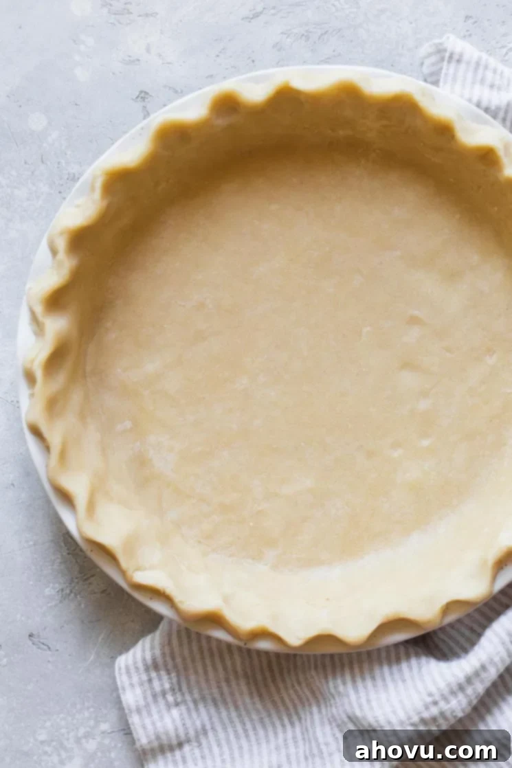 A finished, perfectly golden-brown pie crust in a white ceramic pie dish, resting on a rustic gray wooden surface, ready for filling.