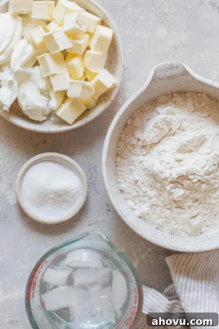 A collection of essential ingredients for making pie crust, including flour, sugar, salt, cubed butter, shortening, and a bowl of ice water, arranged in separate bowls on a gray surface.