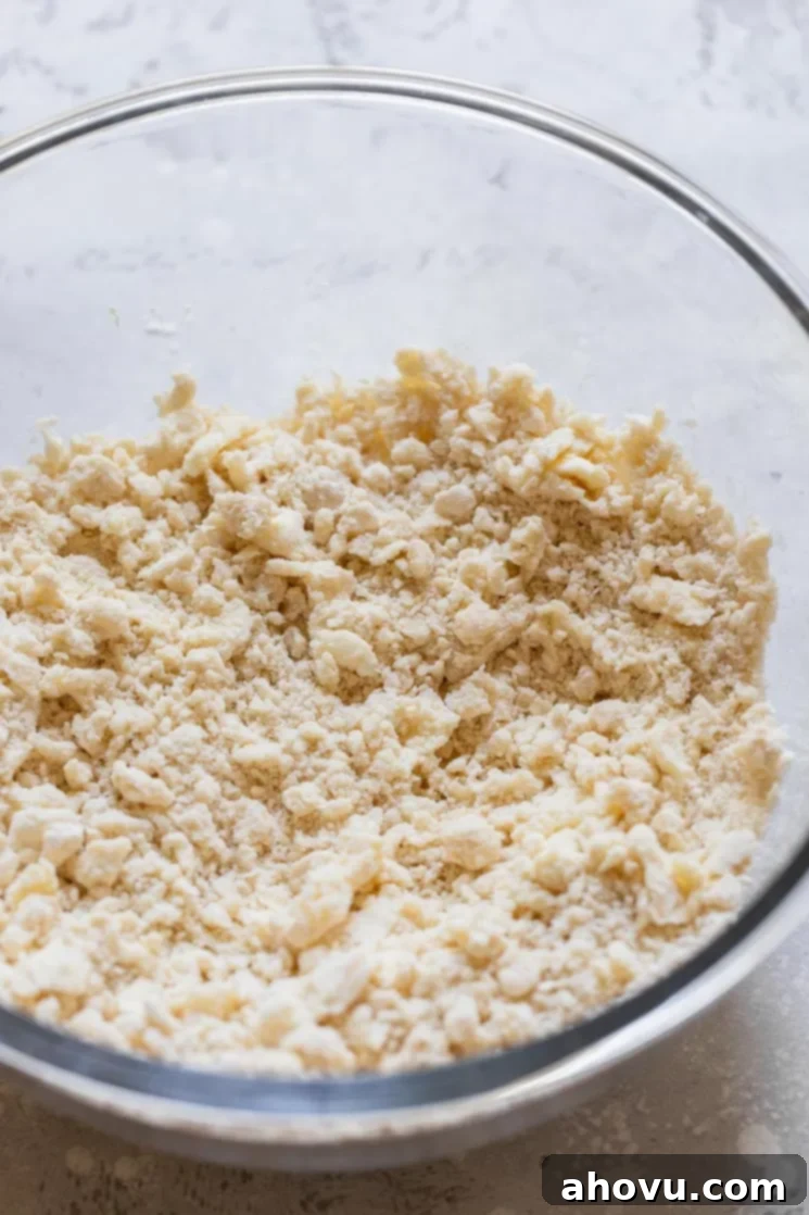 A glass bowl containing dry pie crust ingredients with cubes of cold butter and shortening cut into them, illustrating the initial mixing stage.