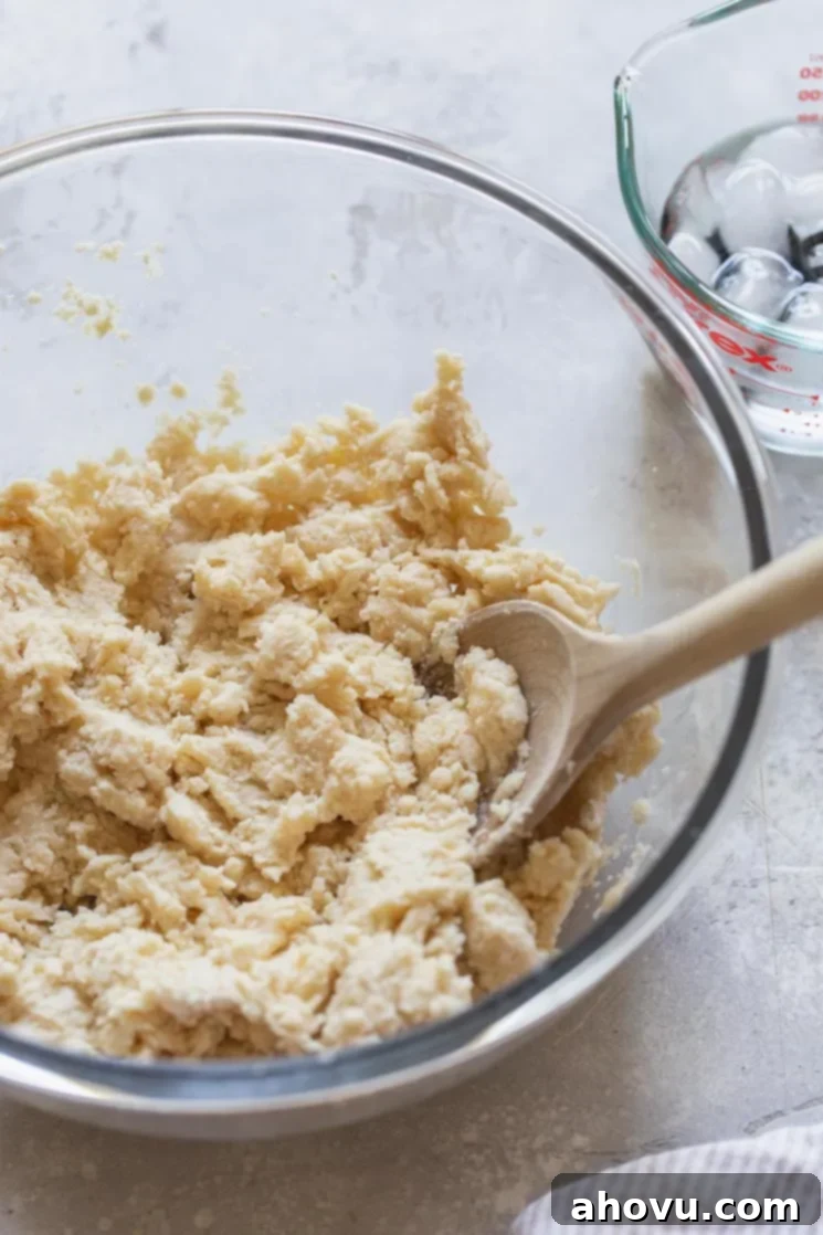 A glass bowl showing the pie crust ingredients after the cold fat has been cut in and some ice water has been added, appearing crumbly yet starting to clump together.