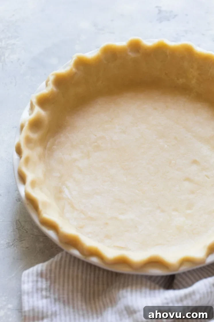 An unbaked pie crust expertly fitted into a white ceramic pie dish, showcasing its beautifully decorated edge, ready for a pie filling.