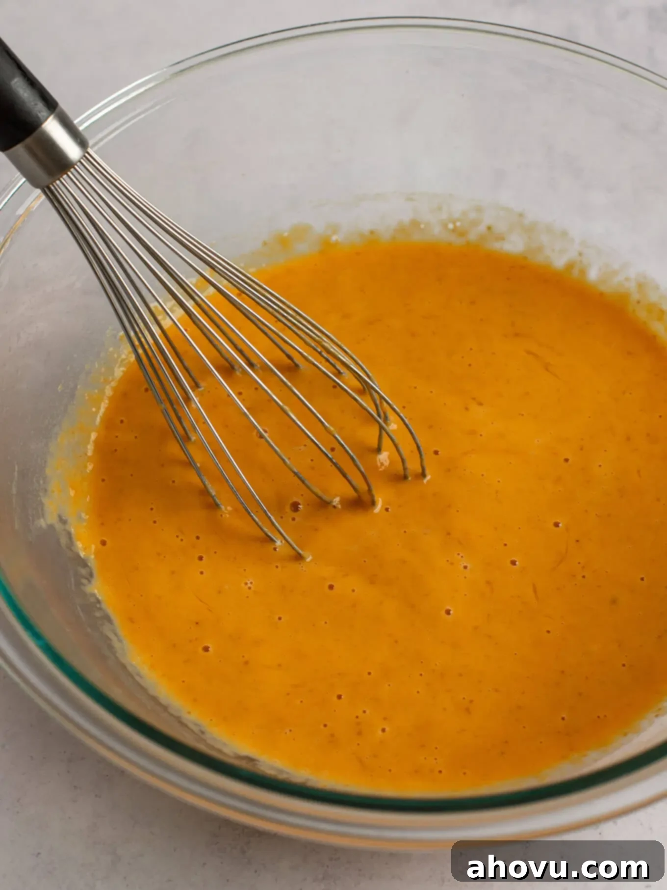 Spiced Pumpkin Perfection 12 The wet ingredients for pumpkin pie, including eggs, pumpkin puree, and evaporated milk, smoothly whisked together in a clear glass mixing bowl.