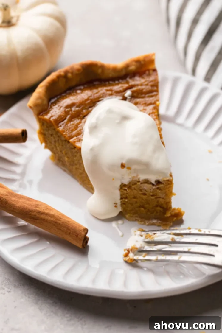 Spiced Pumpkin Perfection 16 A delectable slice of homemade pumpkin pie, generously topped with a swirl of fresh whipped cream, presented on a pristine white plate, ready to be enjoyed.