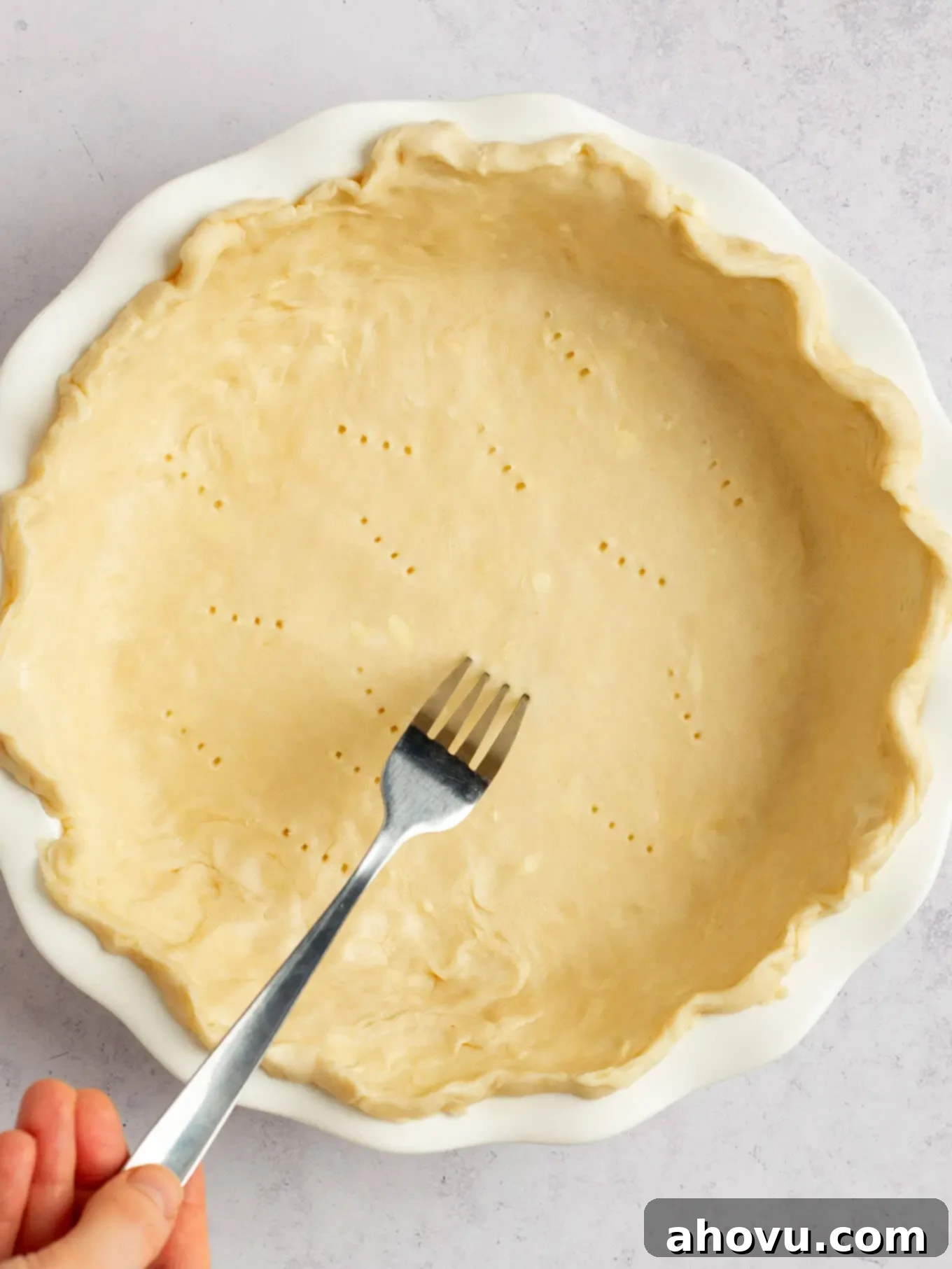 Spiced Pumpkin Perfection 8 An overhead view of a fork being used to carefully prick holes into the bottom of the raw pie crust, a technique known as docking.