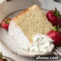 A perfectly portioned slice of chiffon cake, accompanied by vibrant fresh strawberries and a dollop of creamy homemade whipped cream, all served on a pristine white speckled plate, highlighting its elegant simplicity.