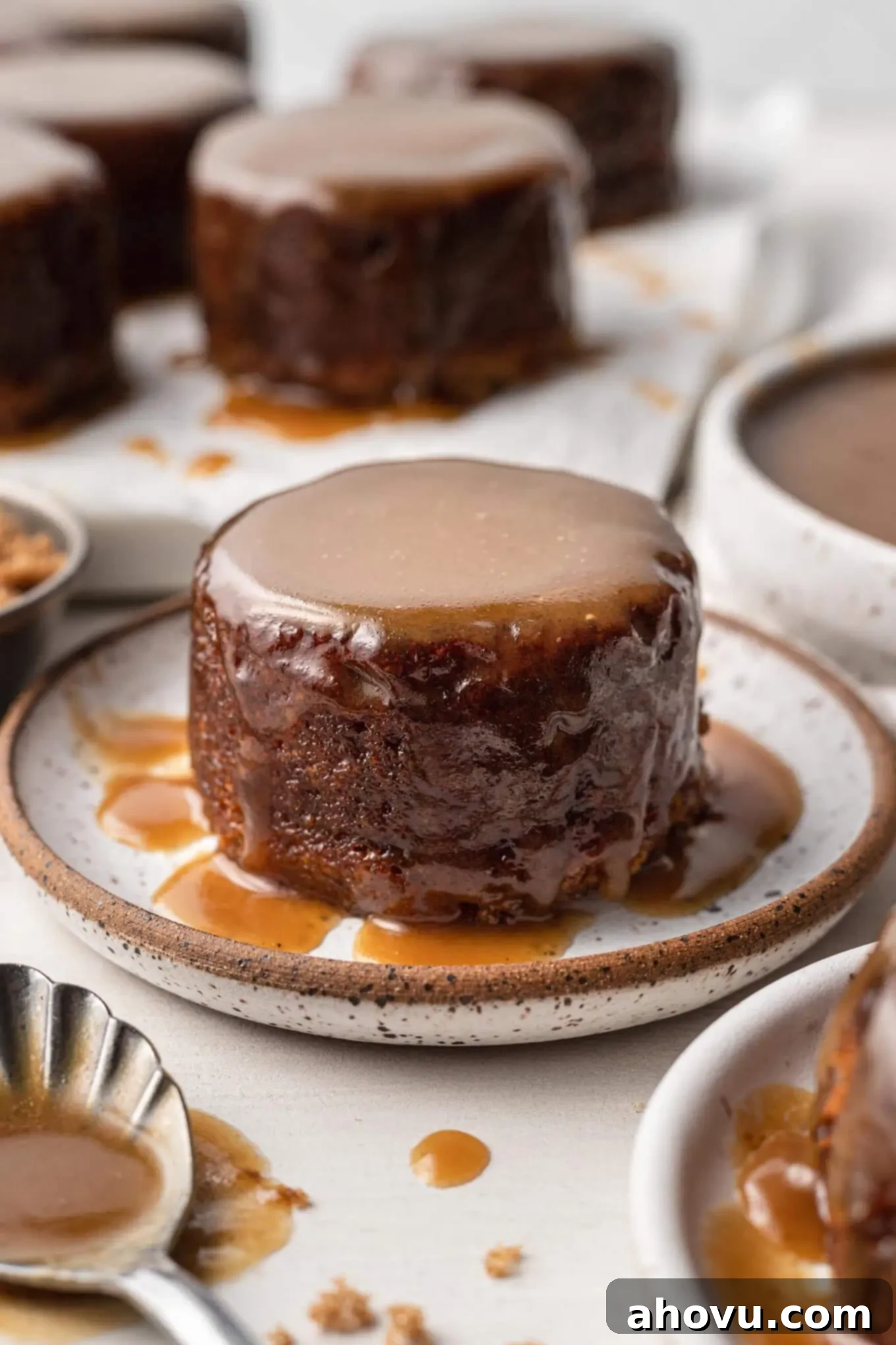 Warm Sticky Toffee Bliss 2 A sticky toffee pudding on a speckled plate. More rest in the background.
