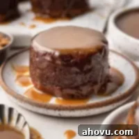 Warm Sticky Toffee Bliss 8 A small round date cake covered in toffee sauce on a white speckled plate.