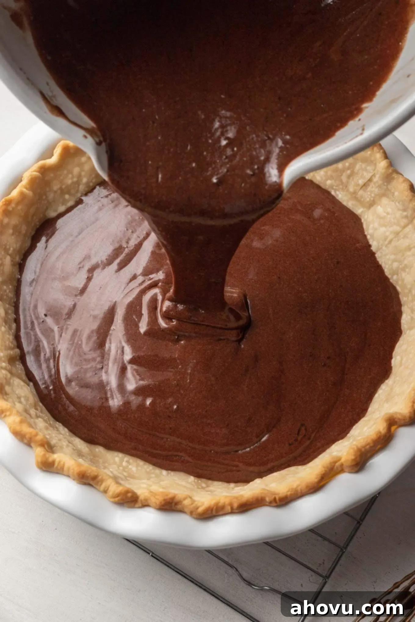 Heirloom Chocolate Pie 5 A steady hand pouring the rich, dark chocolate chess pie filling into a golden, partially baked pie crust in a clear glass dish.