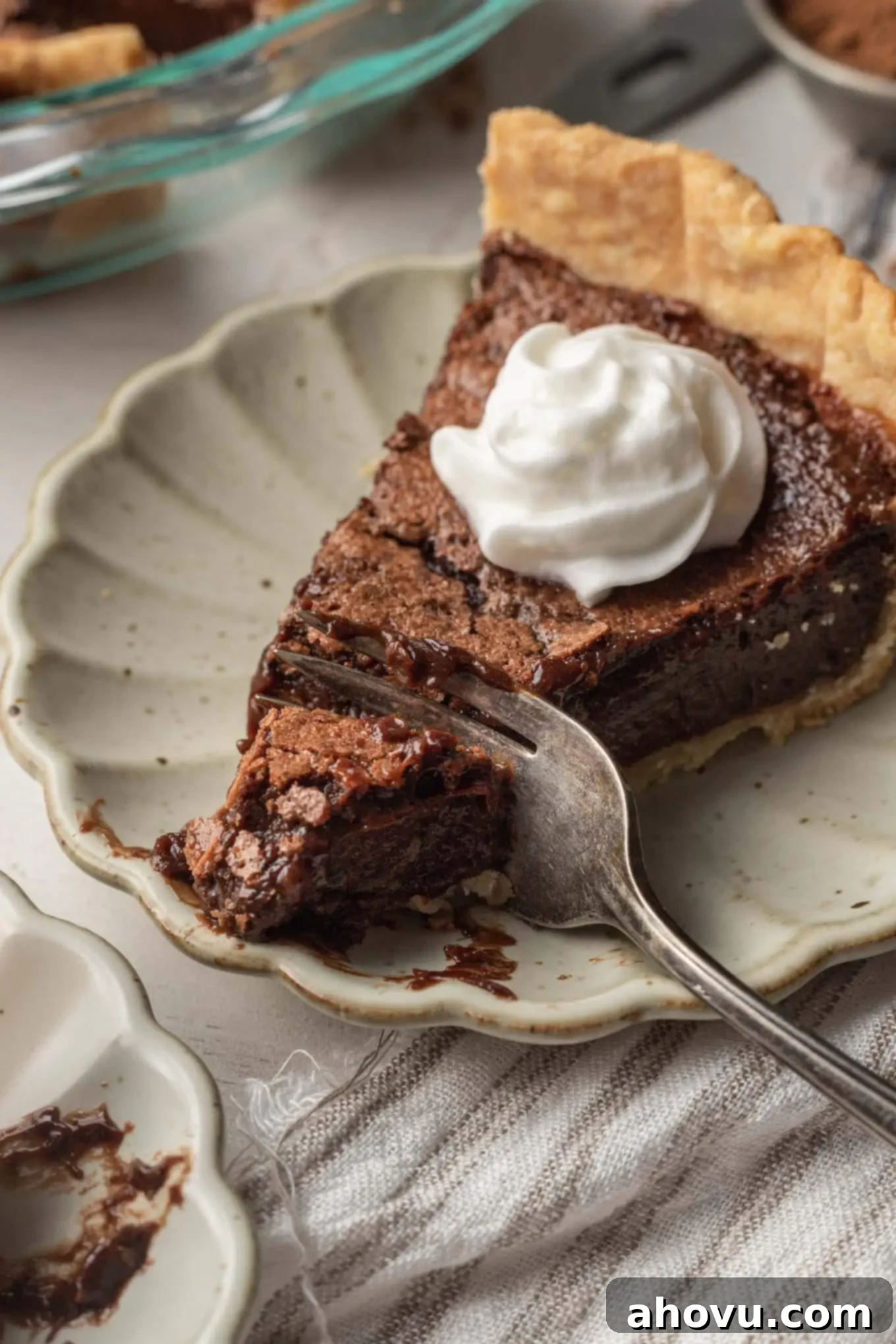 Heirloom Chocolate Pie 7 A close-up shot of a delectable slice of chocolate chess pie, generously topped with fluffy homemade whipped cream. A fork is poised, ready to dig into the delicious pie.