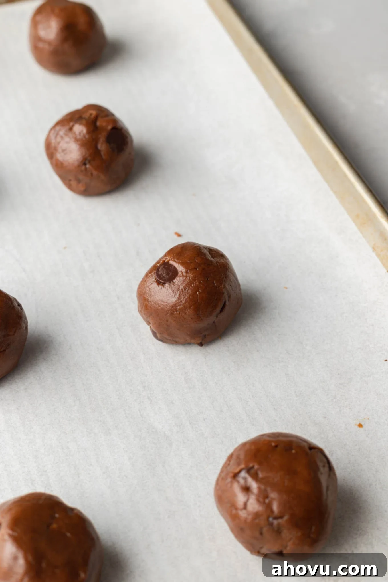 Almond butter cookie dough balls on a parchment paper-lined baking sheet. 