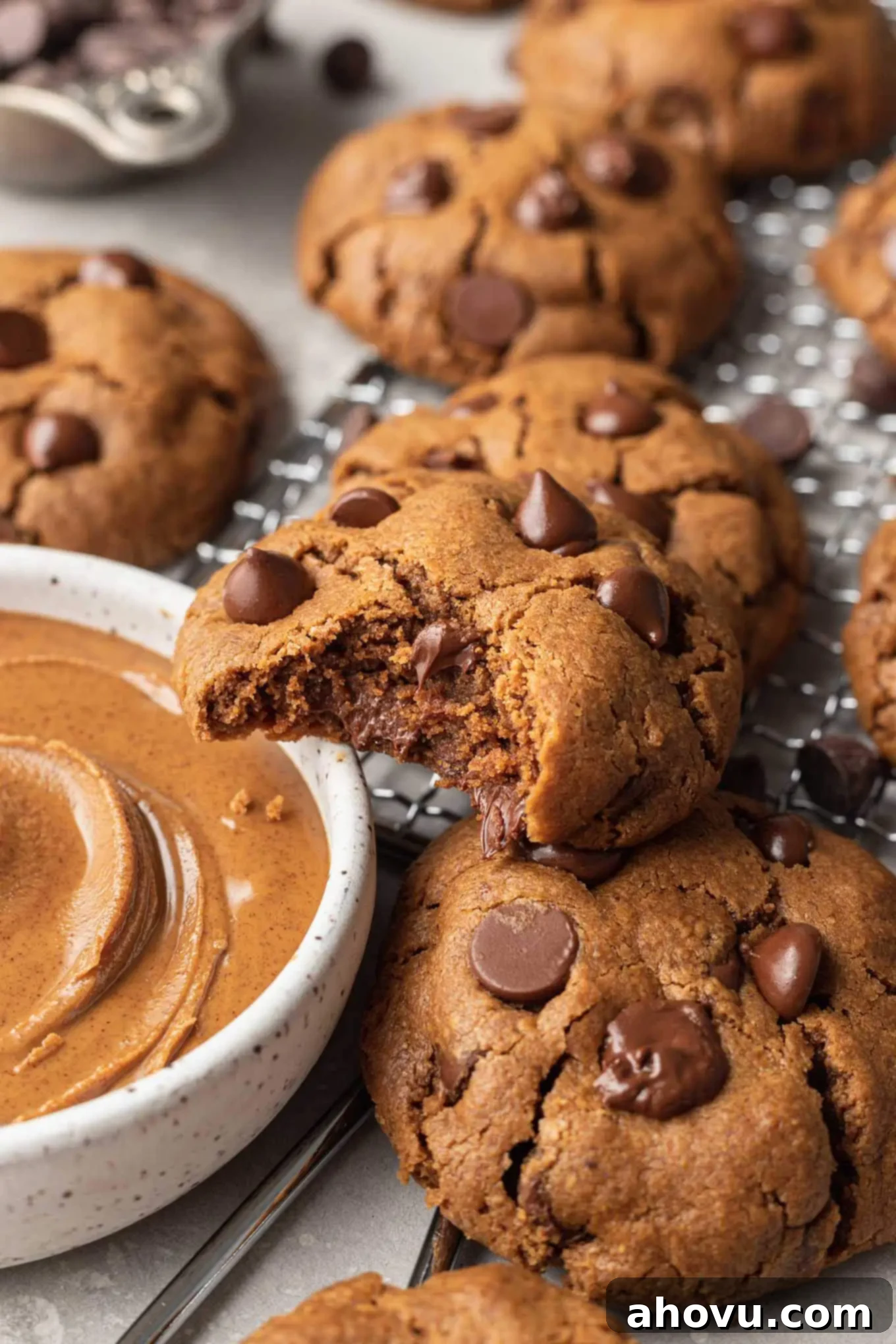A close-up view of a cookie with a bite missing, resting on a dish of almond butter. 