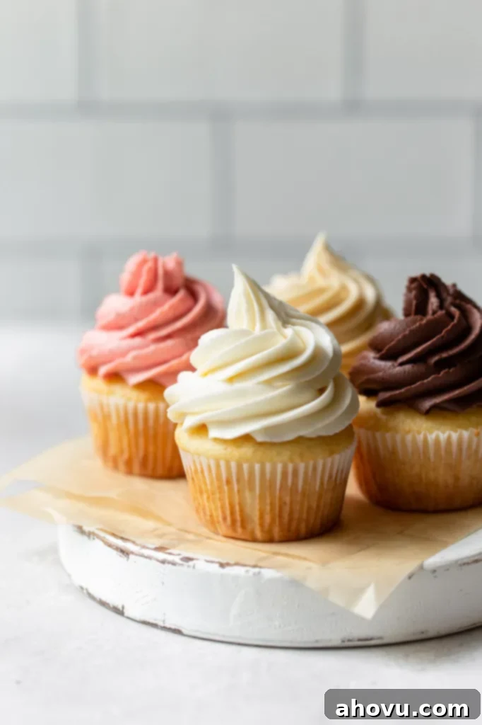 Four cupcakes on a rustic round piece of wood each topped with a different flavor of buttercream frosting.