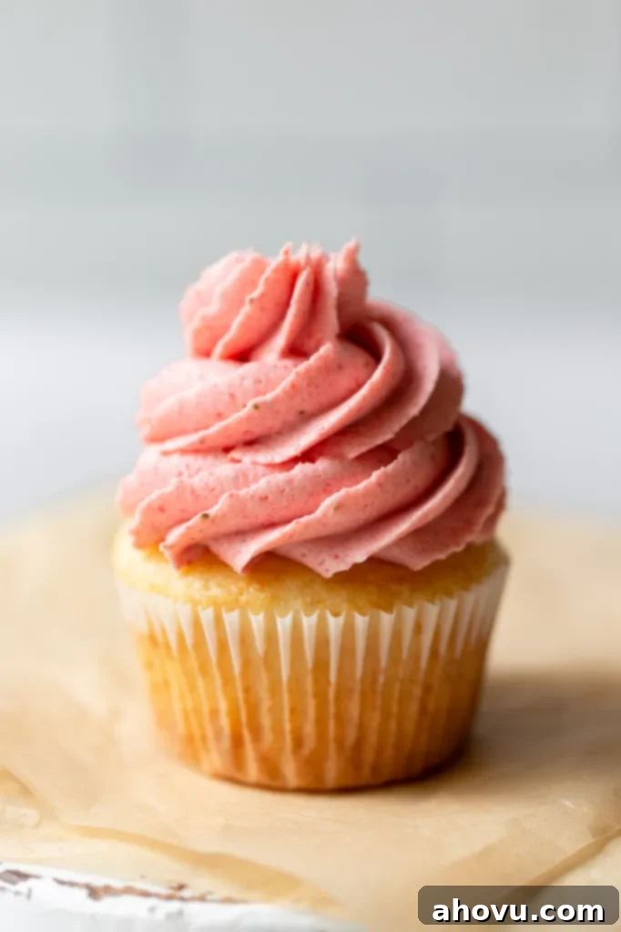 A single cupcake sitting on top of brown parchment paper topped with strawberry buttercream frosting.