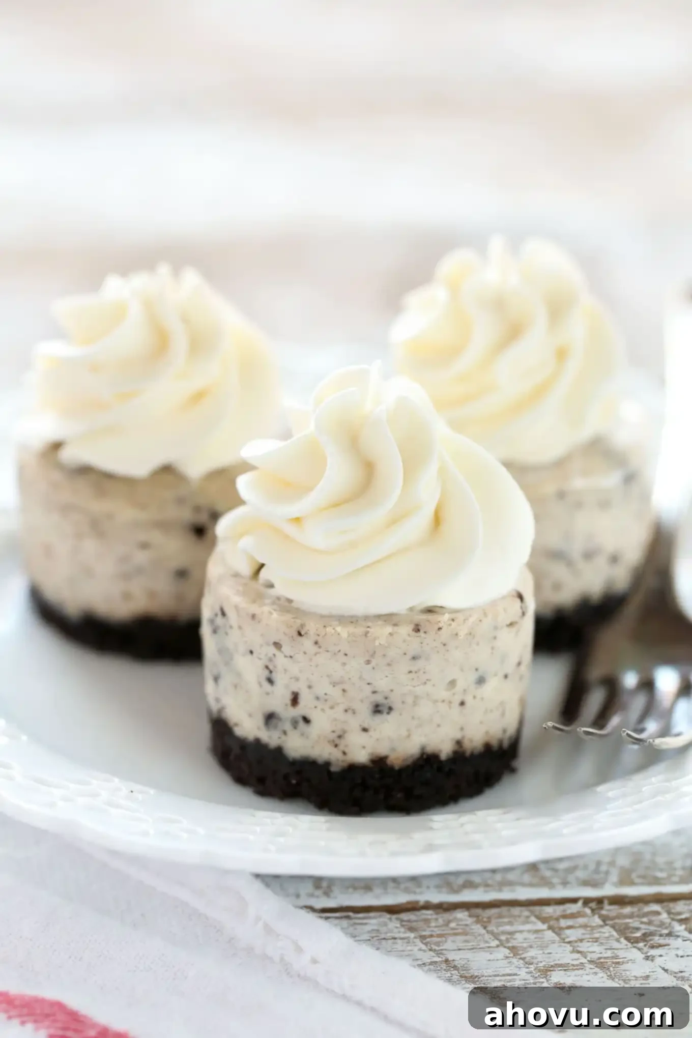Oreo Cookie Cheesecake Bites 3 Close-up of three mini Oreo cheesecake bites on a white plate with a fork, showing the distinct layers and crunchy crust.