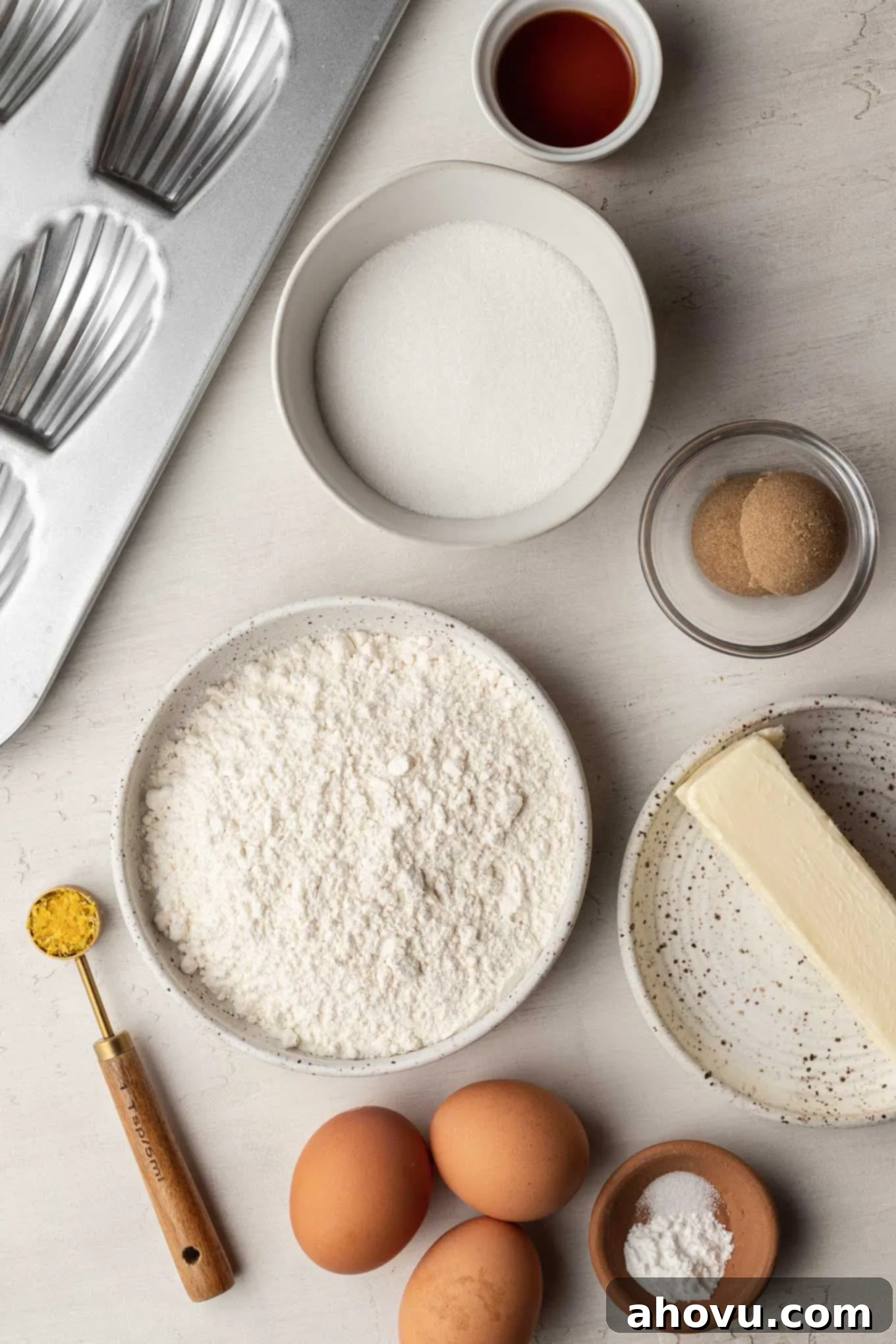 Golden Madeleines 3 An overhead view of the ingredients needed to make French madeleine cookies, including butter, flour, eggs, and sugar.