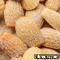 Golden Madeleines 7 Several madeleine cookies dusted with powdered sugar on a piece of brown parchment paper.