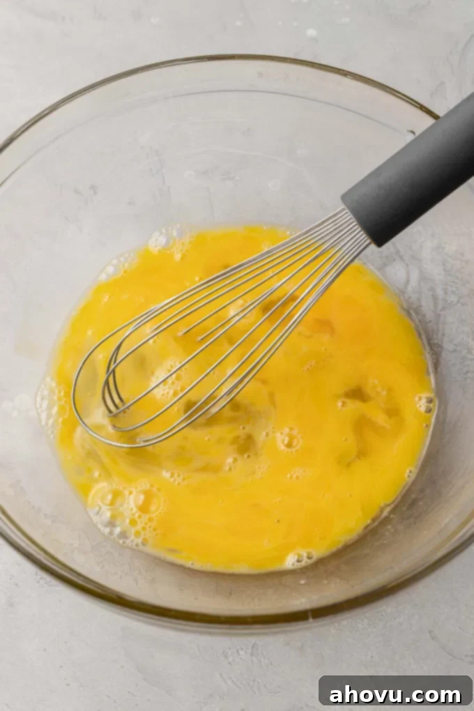 Lightly beaten eggs in a clear glass mixing bowl, ready for the next step of the quiche filling.