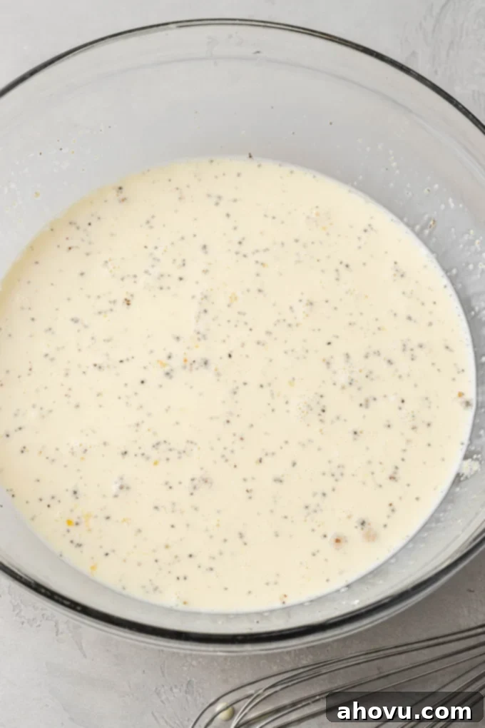The smooth, well-combined egg mixture for a quiche, featuring milk, heavy cream, and spices, whisked together in a glass mixing bowl.