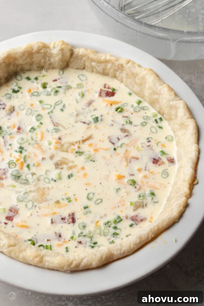 An uncooked quiche, showcasing the creamy egg mixture carefully poured over the vibrant mix-ins in the pie crust, poised for baking.