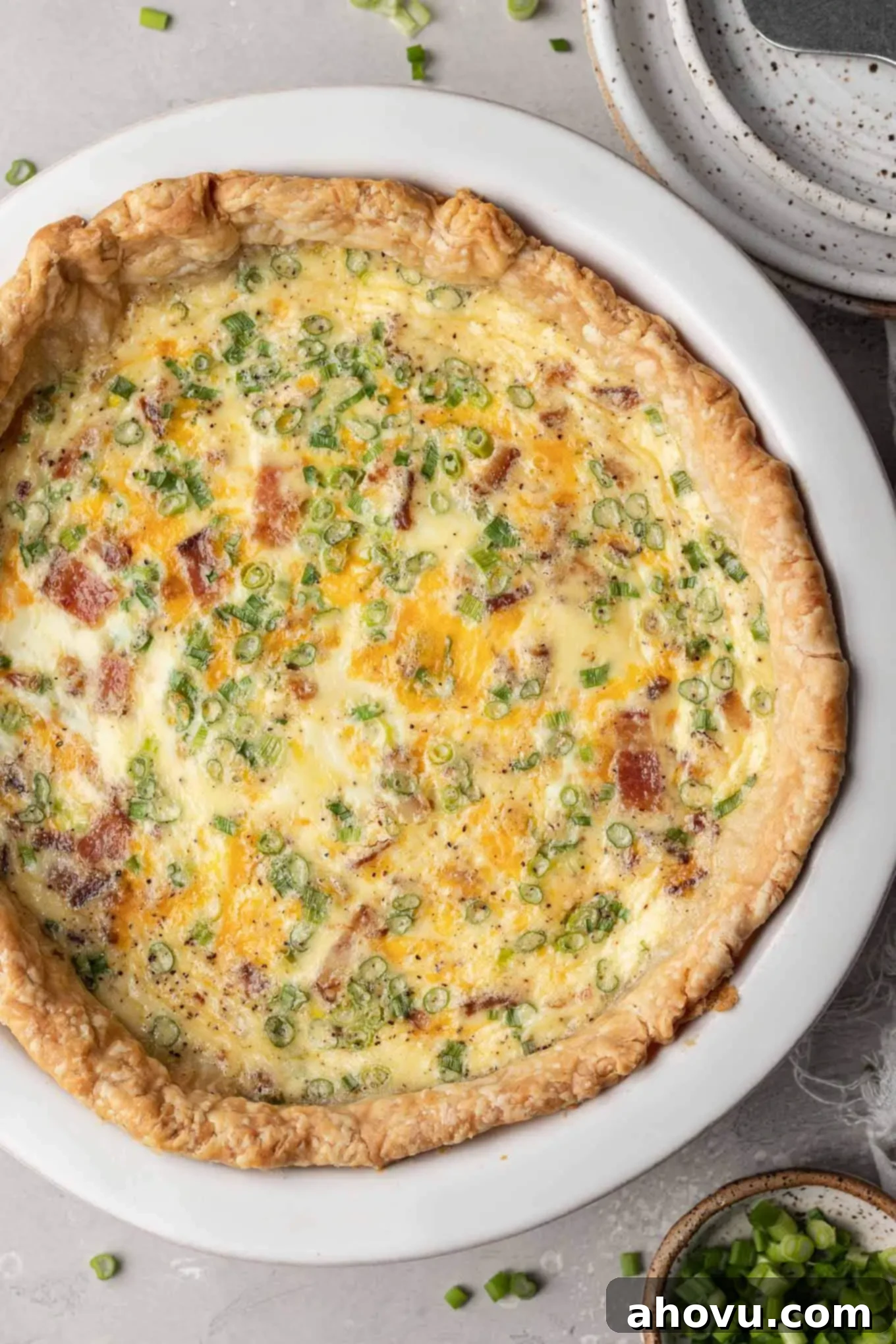 An overhead view of a beautifully baked bacon and cheese quiche, golden brown and perfectly set in a white ceramic pie plate, fresh from the oven.