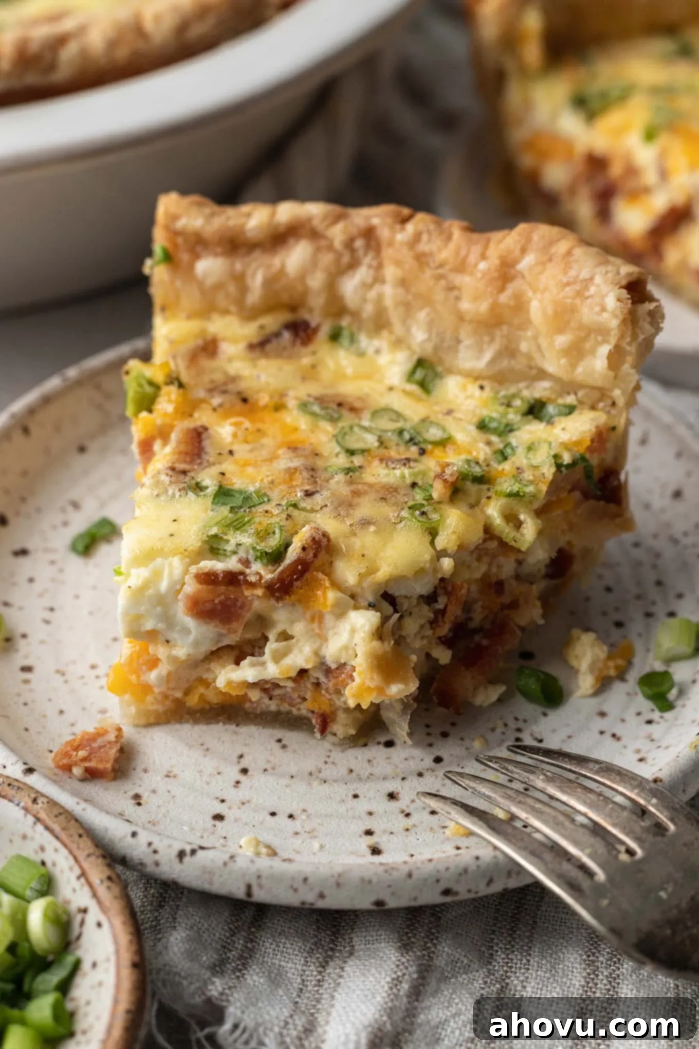 A delectable slice of quiche with a small bite missing, artfully placed on a speckled plate, highlighting its rich textures and inviting flavors.
