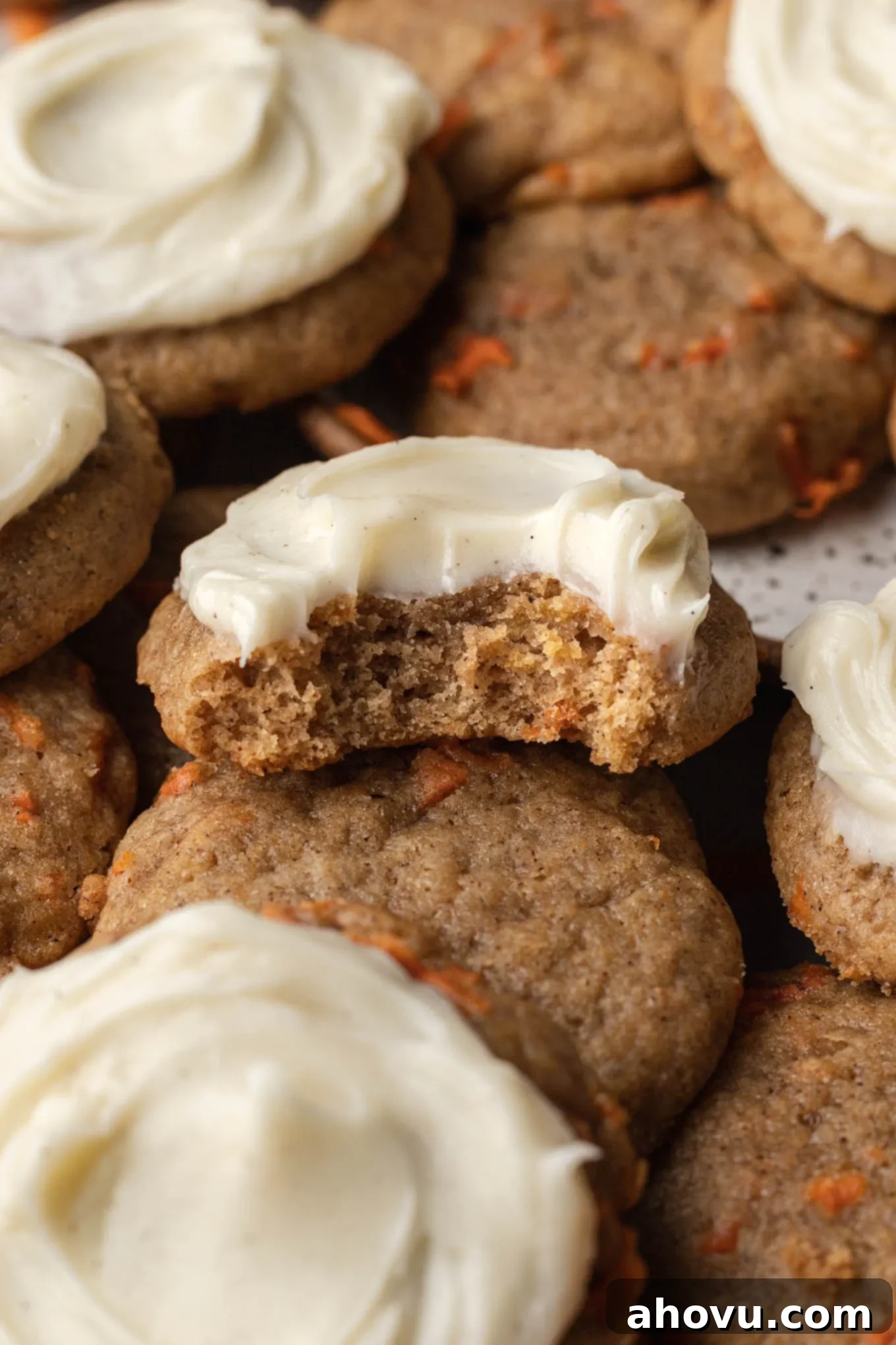 A close-up view of a frosted carrot cake cookie with a bite missing, showing its moist interior and creamy frosting.