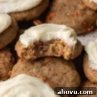 Several frosted carrot cake cookies, with one cookie bitten into, showing the delicious creamy frosting.